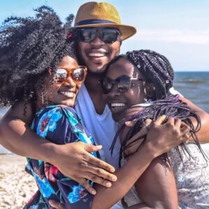 Three friends enjoying a sunny day at the beach, embracing with smiles.